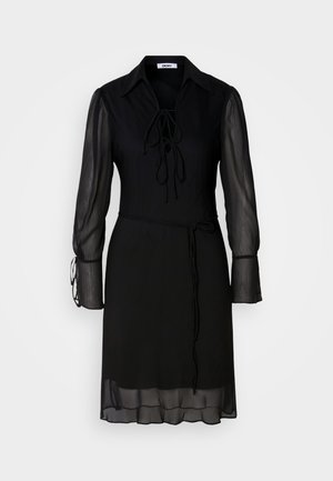 Svart kjole med lange, gjennomsiktige ermer, en knytedetalj i halsen og belte i midjen. Har solid stoff og en flytende silhuett.