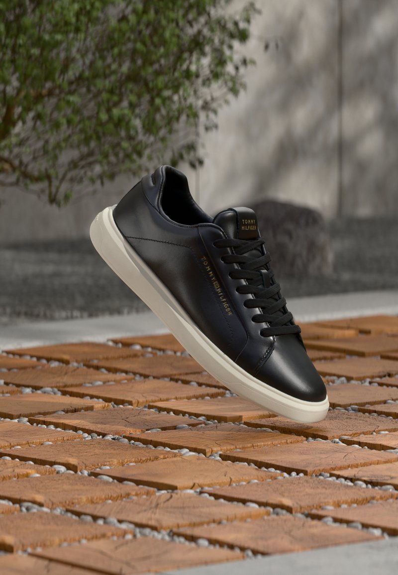 Pantof sport din piele neagră cu șireturi plate, talpă de cauciuc albă și detaliu cu logo auriu. Textură netedă și design clasic cu talpă joasă.