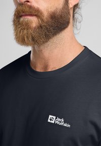 Donkergrijze t-shirt met een ronde hals, voorzien van een wit Jack Wolfskin-logo op de linkerkant van de borst. Gladde stoftextuur.