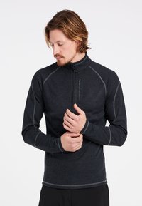 Maglia atletica nera a maniche lunghe con colletto a zip a quarto, presenta cuciture in contrasto grigio e un logo sul petto. Materiale misto poliestere.