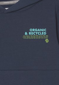 Tissu bleu marine avec du texte bleu clair "Bio & Recyclé" et un texte plus petit jaune concernant le coton biologique et les matériaux en polyester recyclé.