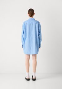 Svetla modra oversized srajca z dolgimi rokavi in vertikalnimi belimi črtami. Ima klasičen ovratnik in zapete manšete. Gladka tekstura tkanine.