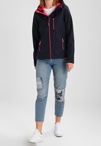 Granatowa kurtka z różowymi akcentami, kieszeniami na suwak i kapturem. Nosi się ją z jasnoniebieskimi dżinsami z naszywkami i białymi trampkami.