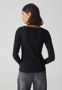 Zwarte geribbelde langemouwen top met een brede halslijn, aansluitende pasvorm en zachte textuur, gecombineerd met hoogtaille grijze jeans.