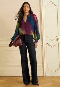 Kolorowa, jedwabna bluzka z bufkami, z przodem na guziki i plisowanym dekoltem. W zestawie z ciemnoniebieskimi, rozszerzającymi się spodniami dżinsowymi oraz burgundową torebką.