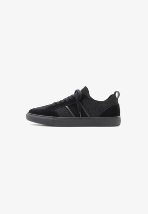 Black sneakers with a mesh upper and suede accents. Features flat laces, a rounded toe, and a thick rubber sole for durability.