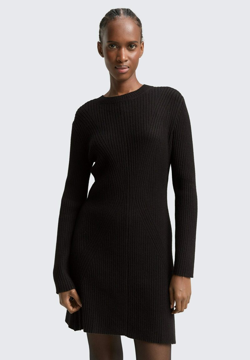 Schwarzes geripptes Strickkleid mit langen Ärmeln, rundem Halsausschnitt und strukturiertem Muster. Figurbetonte Silhouette, die sich an der Taille verjüngt, leicht über dem Knie.