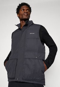 Schwarze Pufferweste mit hohem Kragen, vorderen Taschen und Knöpfen. Mit einem weißen Logo auf der linken Brust. Hergestellt aus wasserabweisendem Material.