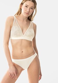 Bralette en dentelle avec des bonnets triangulaires, des bretelles en tulle transparent et une bande élastique. Bikini sans coutures assorti en couleur crème clair, au design minimal.
