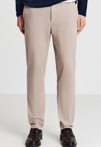 Pantaloni beige con una trama liscia, design a gamba dritta e tasche anteriori piatte. Abbinati a mocassini scuri, senza motivi visibili.