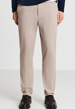 Pantalons beiges avec une texture lisse, une coupe droite et des poches avant plates. Assortis à des mocassins foncés, sans motifs visibles.