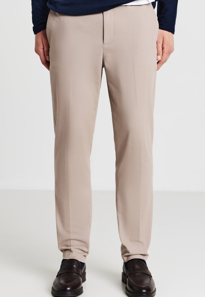 Pantaloni beige con una trama liscia, design a gamba dritta e tasche anteriori piatte. Abbinati a mocassini scuri, senza motivi visibili.