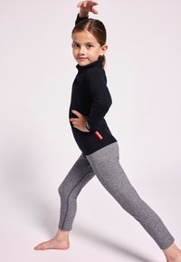 Top negro de manga larga con cuello alto y logo, combinado con leggings grises con detalles en las costuras laterales. Pose descalza con las manos levantadas.
