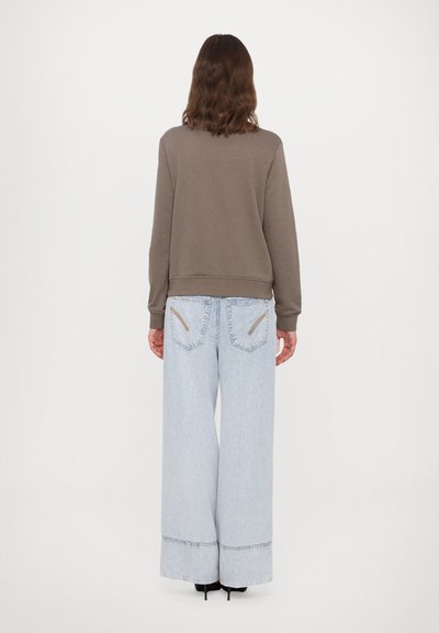 Brun sweatshirt med en cropped design, paret med lys blå vide bukser med skrå baklommer og en frynset kant.