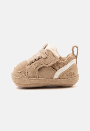 Baskets en daim beige pour tout-petit avec lacets en tissu, doublure douce, languette de tirage et un détail blanc près du talon avec logo UGG estampé.