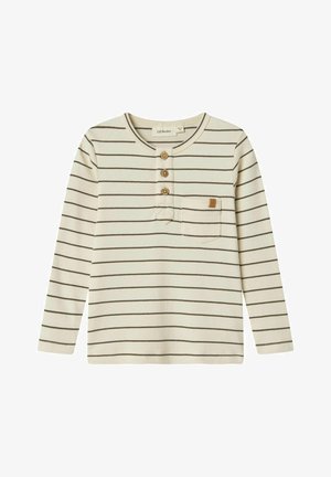 Ilgi piedurkņu organiskā kokvilnas krekls krēmkrāsā ar plānām brūnām horizontālām svītrām. Iespējo trīs koka pogas un kreisajā krūtīs ir kabata.