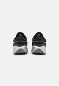 Des chaussures de sport noires avec un dessus en tissu lisse, un talon texturé et des accents argentés sur la semelle. Elles disposent d'une languette pour un enfilage facile.