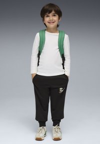 Witte langekoot shirt, zwarte trainingsbroek met een kikkerafbeelding, en een groene rugzak. Beige sneakers met groene en bruine accenten.