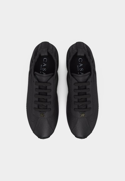 Ζευγάρι μαύρα δερμάτινα sneakers με υφή, κορδόνια, ελαστικό κολάρο και μικρό μεταλλικό λογότυπο, σε θέα από πάνω σε λευκό φόντο.