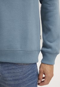  Lichtblauwe sweatshirt met ribgebreide boorden en zoom; zachte textuur; klein "BLEND" label nabij de zoom; gedragen met denim jeans.