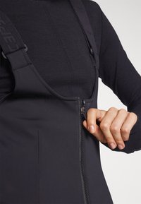 Svart glidelås bodysuit med justerbare stropper, som har en glatt tekstur, strukturert design og en tettsittende passform. Glidelås foran for enkel tilgang.