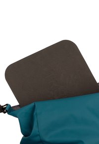 Un coussin en mousse noir rectangulaire partiellement inséré dans un sac à dos d'extérieur bleu avec un clip visible sur le côté.