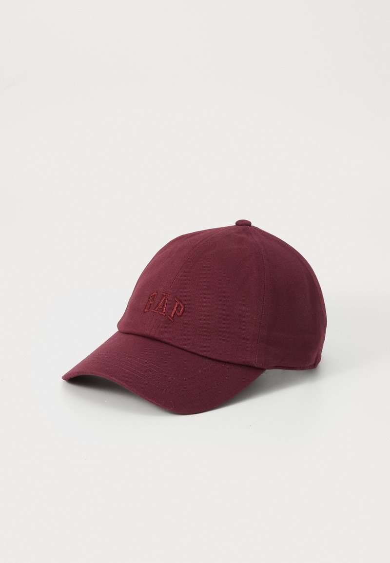 Mørkebrun bomullslue med buet skjerm og brodert "GAP"-logo foran. Har sydd ventilasjonsøyne og en avrundet krone.