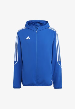 Veste de sport bleue avec des bandes blanches sur les manches, fermeture éclair intégrale à l'avant, capuche et petit logo blanc sur la poitrine.