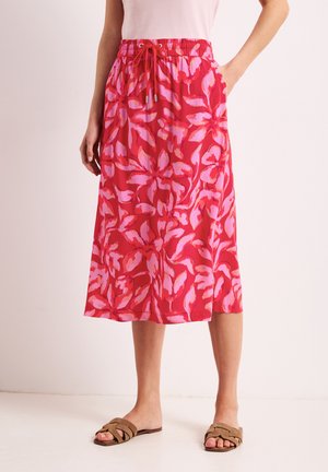 Rødt midi-nederdel med pink blomsterprint, elastisk talje med snøre, brugt med beige slip-in sandaler og en lyserød top.