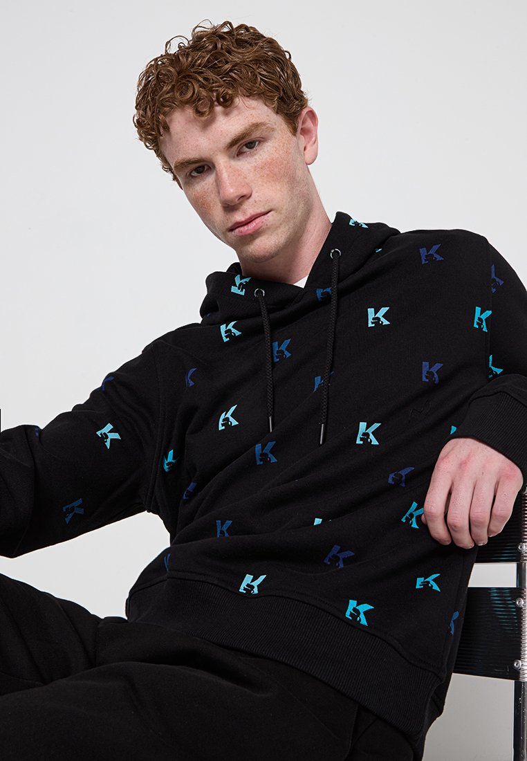 Haut à capuche noir en tissu doux, avec un motif de logo multicolore en bleu et bleu foncé, doté d'une poche kangourou et d'une capuche avec cordon.
