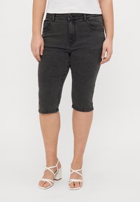 Bermudas de mezclilla negra con tiro alto, diseño de cinco bolsillos y dobladillo vuelto, combinadas con sandalias blancas de tacón bloque y tiras.