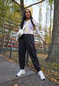 Svart sweatpants med avslappnat snitt, långärmad topp i lila och gult tie-dye med vågig nederdel, vit crossbody-väska och vita joggingdojor med detaljer.
