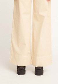 Pantaloni beige a gamba larga realizzati in un tessuto morbido, con orlo pulito e abbinati a scarpe con piattaforma nere.