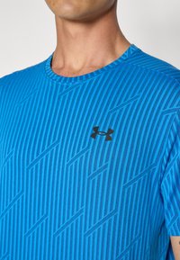 Blå atletisk t-skjorte med rund hals, med et stripete mønster i varierende nyanser, og en liten svart Under Armour-logo på brystet.