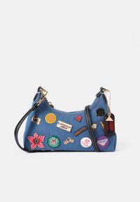 Denim axelväska med svart rem, prydd med olika färgglada lappar och nålar, inklusive hjärtan, logotyper och en blommig design.