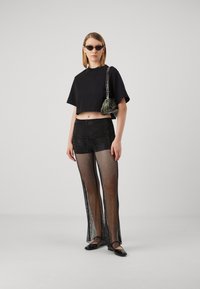 Maglietta nera corta, pantaloni in rete nera trasparente con fessure laterali e ballerine nere. Gli accessori includono una piccola borsa a fantasia verde e occhiali da sole.