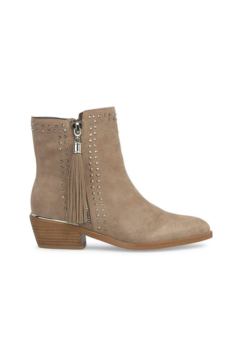 Bota de tobillo de ante beige con un tacón bajo, acentos de tachuelas a lo largo del costado y un borlas decorativa fijada a la cremallera.
