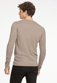 Ljusbrun långärmad tröja med texturerad yta, rund halsringning och ribbade muddar. Bärs med svarta byxor och visar en figurnära silhuett.