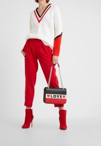 Červený a bílý žebrovaný svetr s výstřihem do V, v kombinaci s červenými plisovanými kalhotami. Černá a �červená kabelka se grafickým nápisem "LOVE" a stříbrným řetízkovým popruzním.