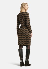 Langlijfjurk met een chevronpatroon in zwart en metallic goud, getailleerde silhouet, tot de knie, gecombineerd met zwarte laarzen tot de knie.