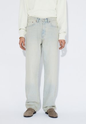 Hellblaue Jeans aus Denim mit lockerem Sitz und geradem Bein. Verfügen über fünf Taschen, Nähte und leichte Used-Effekte. Getragen mit einem leichten Pullover.