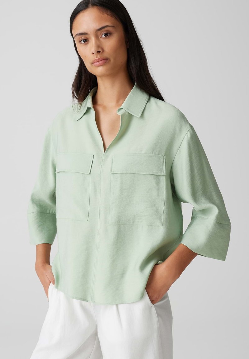 Camicia collare verde chiaro con due tasche frontali, maniche a tre quarti e vestibilità rilassata, realizzata in tessuto morbido con una finitura testurizzata.