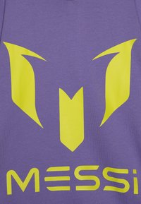T-shirt violet avec un grand logo jaune ayant des formes pointues et le mot "MESSI" en lettres jaunes en gras en bas.