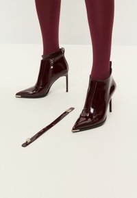 Bottes de cheville en cuir verni bordeaux avec des pointes aiguisées et un talon aiguille haut. Elles sont dotées d'une fermeture éclair sur le côté et d'une sangle assortie amovible.