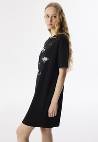 Zwarte jurk met korte mouwen, gemaakt van zachte stof, met witte grafische ontwerpen aan de voorkant, een relaxte pasvorm en een lengte boven de knie.