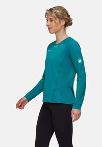 Langärmliges, teal-farbenes Sportshirt mit Rundhalsausschnitt, strukturiertem Stoff und kontrastierenden Nähten; Logo auf dem Ärmel und reflektierende Akzente.