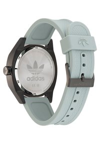 Montre ronde en acier inoxydable noir avec un bracelet en silicone bleu clair ; présente le logo Adidas sur le cadran et un motif texturé sur le bracelet.