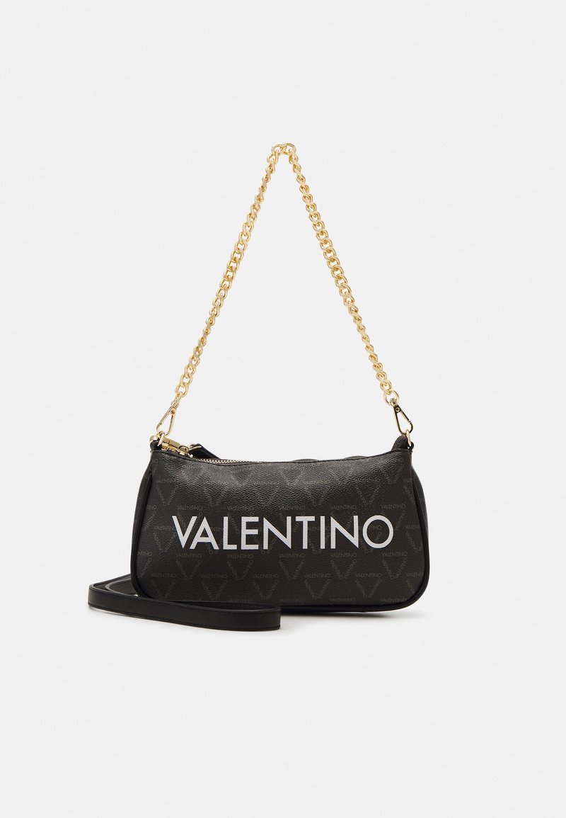 Svart läderhandväska med ett guld kedjestrap, dragkedjestängning och iögonfallande vit "VALENTINO"-logotyp. Texturerat mönster av små logotyper.