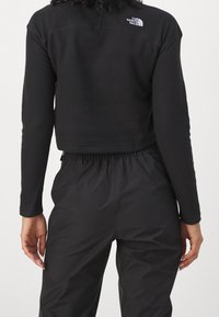 Schwarzes, kurzes Sweatshirt mit langen Ärmeln und einem viertel Reißverschluss, ausgestattet mit einem Logo auf dem Rücken und einem elastischen Bund.