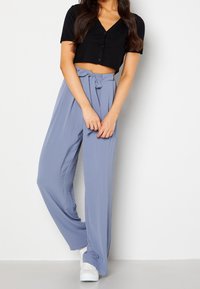 Svart kortärmad cardigan med knappar, kombinerad med ljusblå högmidjade byxor med bindebälte. Slät textur, design med vida ben.